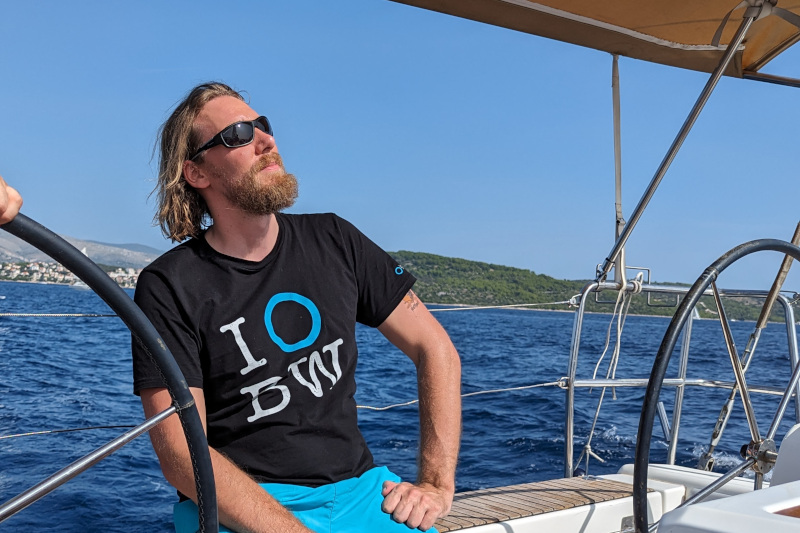 Mike Gebert at the helm in sunglasses, looking ahead while sailing
