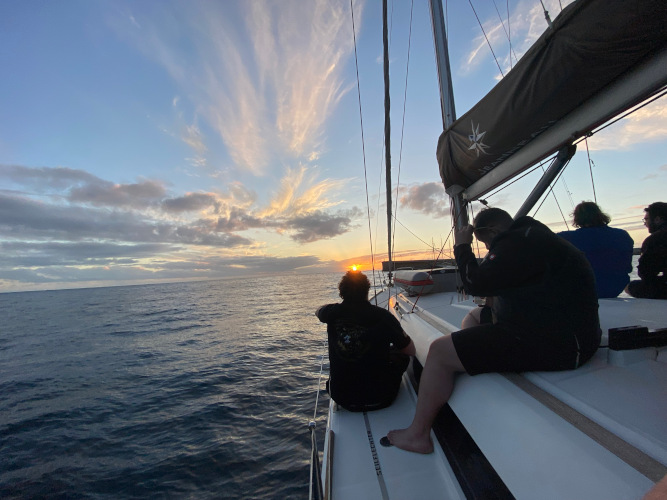 Crew sitting on the foredeck watching a golden sunset at sea