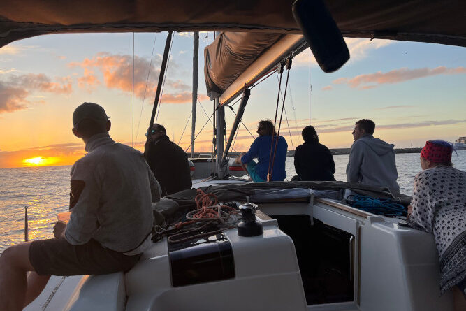 Crew gathered in the cockpit watching a sunset over the sea